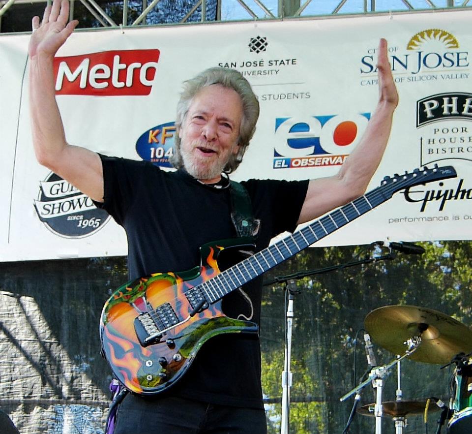 Harvey Mandel raises both arms onstage with a flame painted electric guitar hanging at his waist